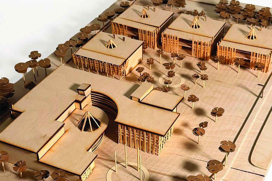 Wooden architectural model displaying a campus with geometric buildings, scattered trees, and pathways. 
