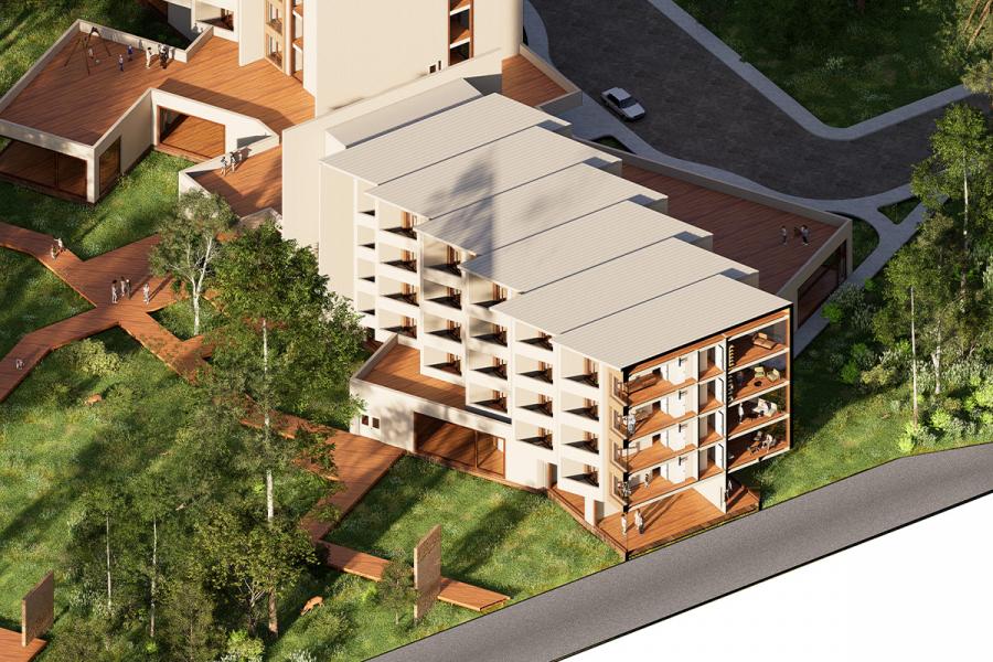 Aerial view of a modern apartment building with beige walls, multiple balconies, and a wooden walkway. Surrounded by lush greenery and trees, and adjacent to a road.