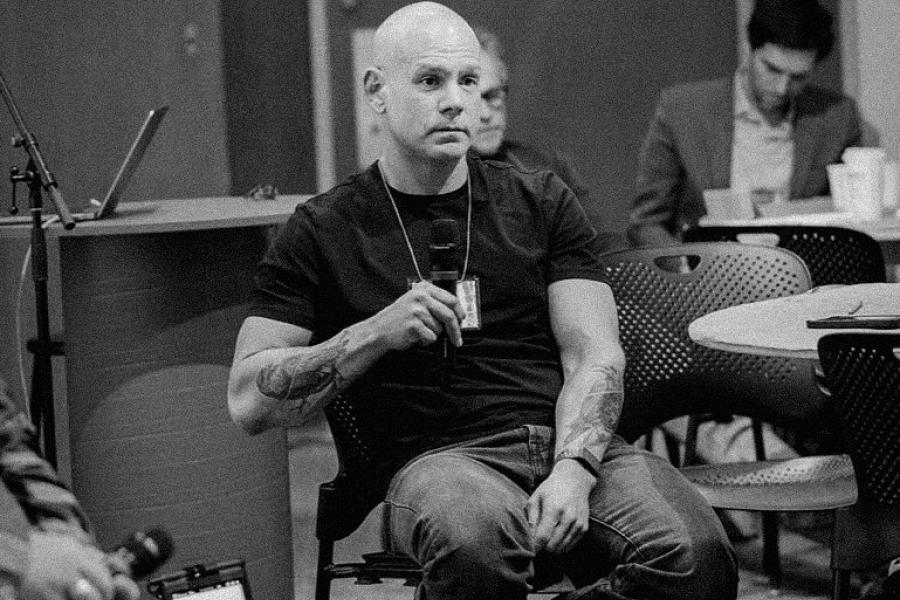 Black-and-white photo of Shawn Bailey seated in a classroom, holding a microphone; people sit behind him, engaging in discourse.