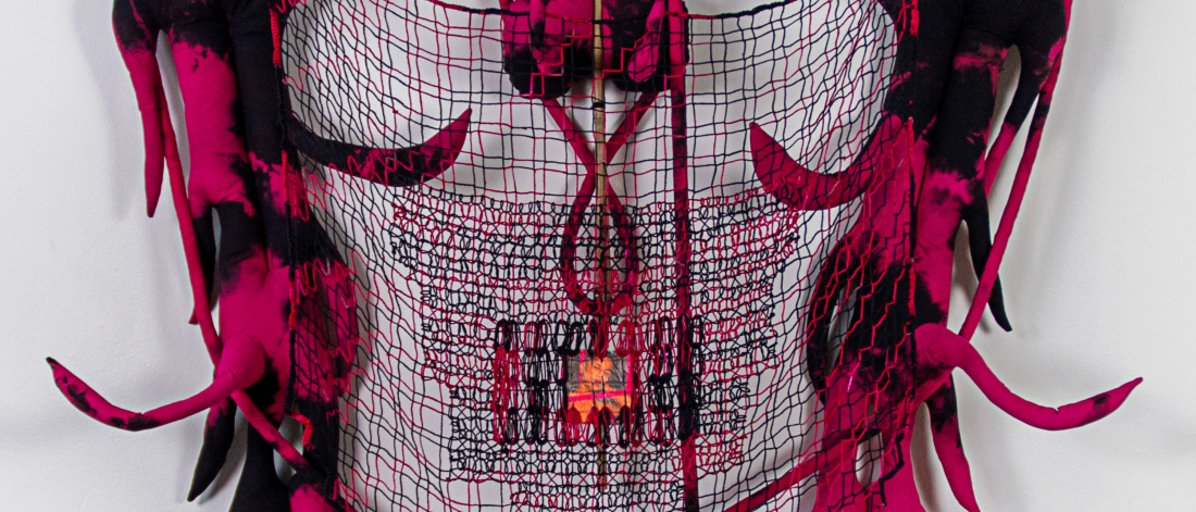 A sculptural textile with black and pink fabric, wire grid base, and glowing central element, resembling horns or tendrils extending outward.