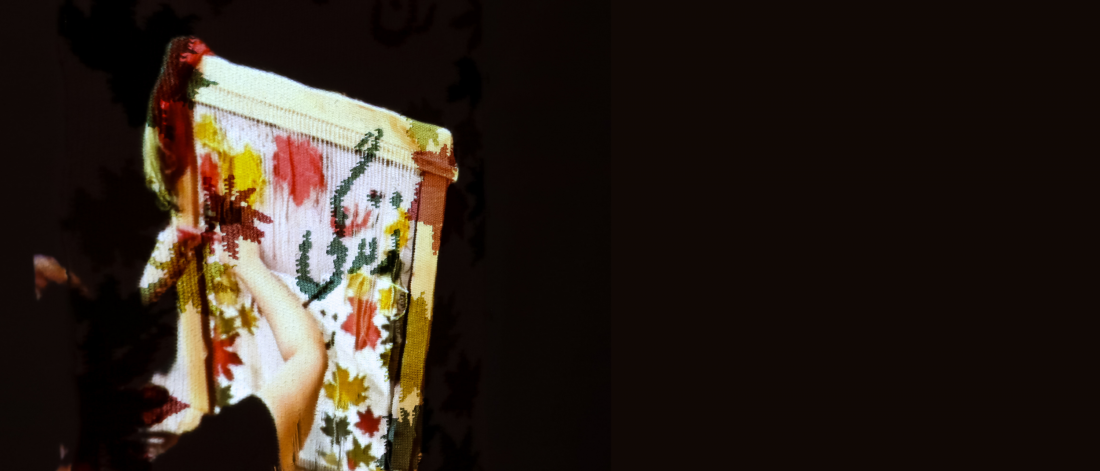 A projected image of floral patterns and text overlays a person holding a textile, partially obscured in shadow.