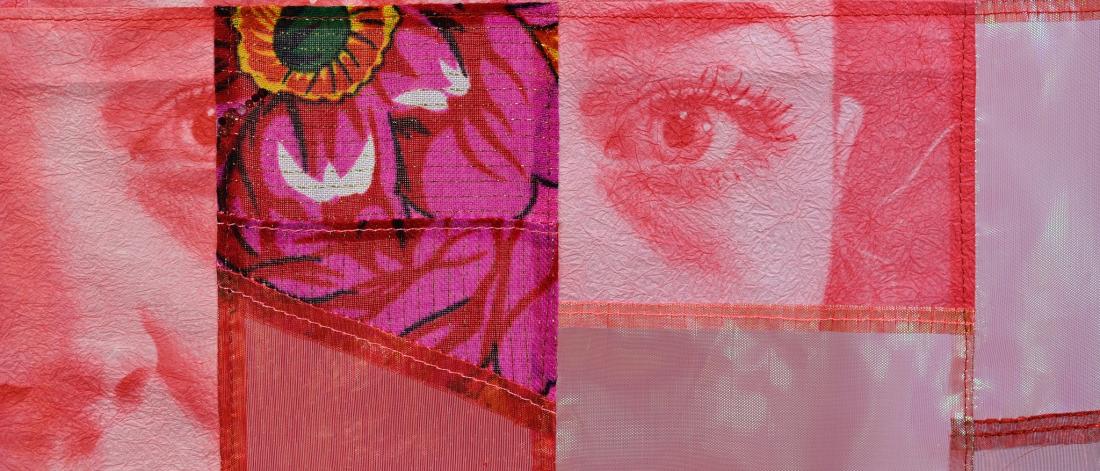 A close-up of a neon pink textile portrait showing a woman’s face and floral patterns pieced from synthetic fabrics and ribbons.