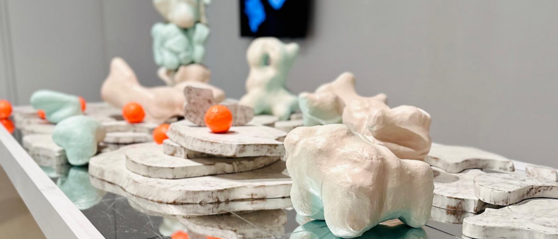 Interactive sculptural installation of pastel forms and bright orange balls displayed on a mirrored table.