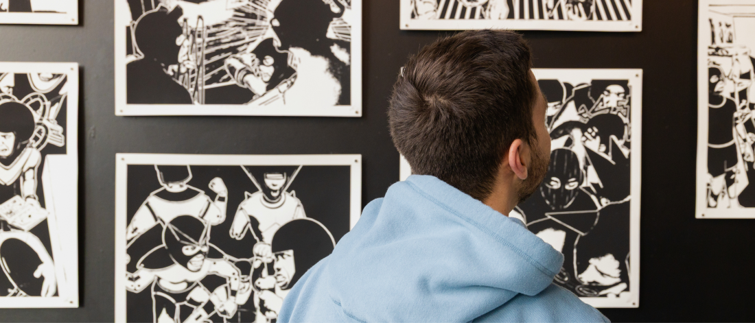 Visitor in a light blue hoodie views a wall of black-and-white graphic artworks displayed in a gallery exhibition.