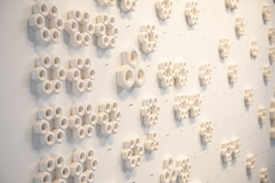 A series of hexagon shaped ceramic pieces, hung organically interlocking on a wall.