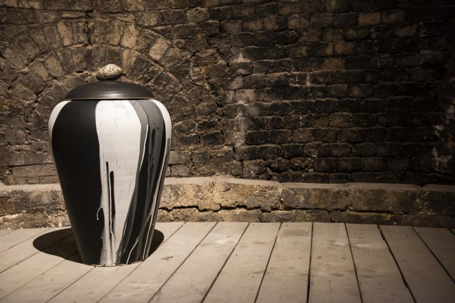 A black and white ceramic lidded vase sits on an old wood floor.