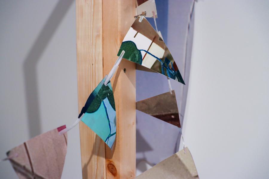 A freestanding wooden frame supporting fragmented collage pieces and dangling triangular paper bunting.
