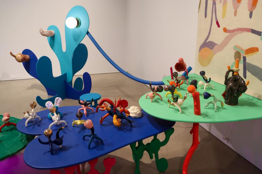 A colorful arrangement of ceramic figurines displayed on interconnected blue and green tables with abstract legs.