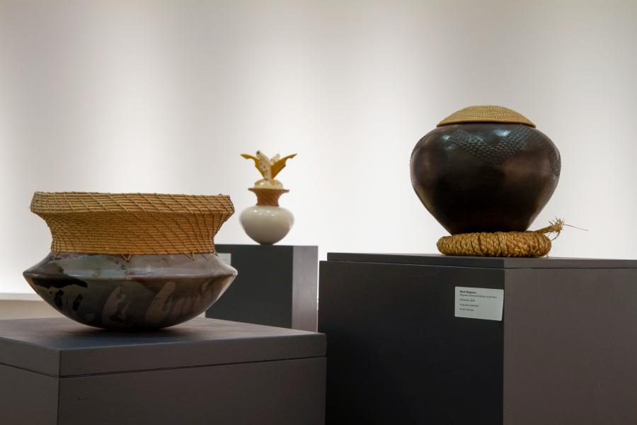 A group of ceramic vessels with woven and textured details, arranged on pedestals in a well-lit gallery space.