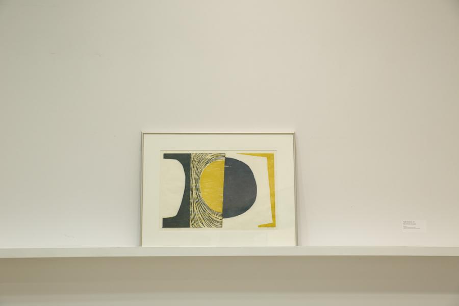 A framed artwork displaying minimal abstract shapes in black and yellow on white paper.