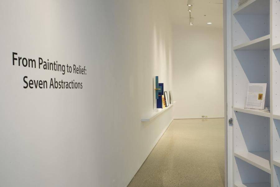 Entry view of the exhibition, with the title “From Painting to Relief: Seven Abstractions” displayed on the wall and a row of colorful abstract works in the distance.