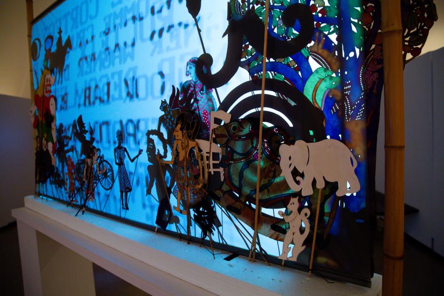 Close-up of a shadow puppet-style display with intricate cut-outs and vivid blue backlighting.