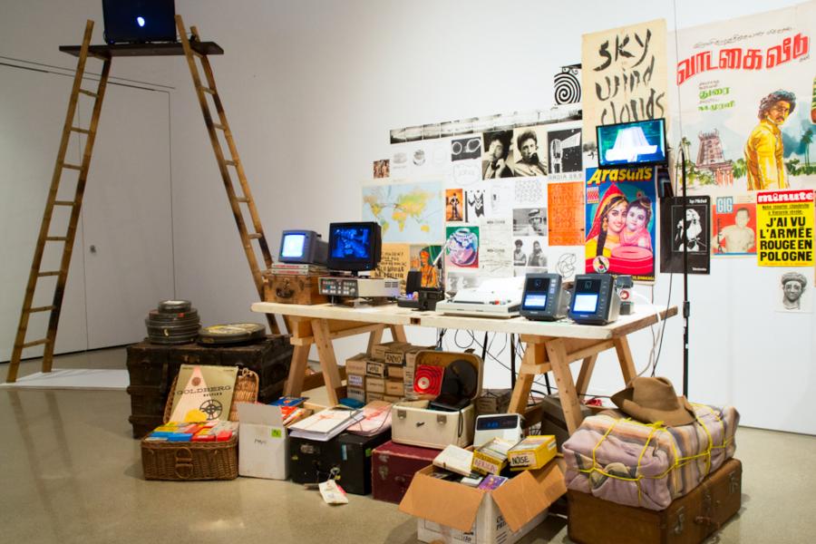 A detailed view of a table filled with vintage objects, posters, typewriters, and monitors, with a tall wooden ladder propped against the wall.