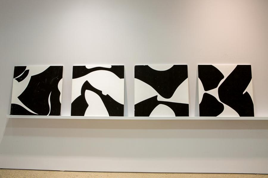 A row of five abstract black-and-white paintings resting on a slim white shelf, featuring organic, curving shapes in high contrast.