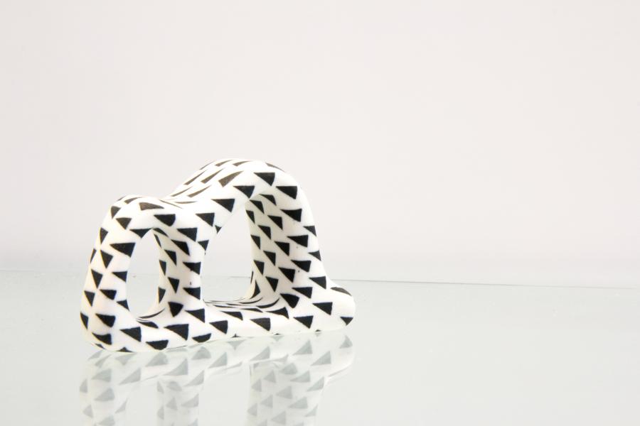 A small black-and-white abstract ceramic sculpture with triangle patterns on a reflective surface.