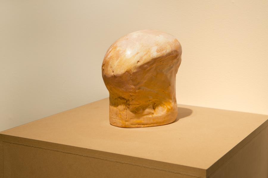 A close-up view of a single organic golden sculpture with a textured, rounded surface, displayed on a pedestal.