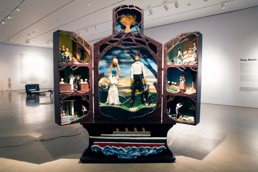 A large sculptural triptych with figurative dioramas depicting various narratives, placed in the centre of a gallery space.