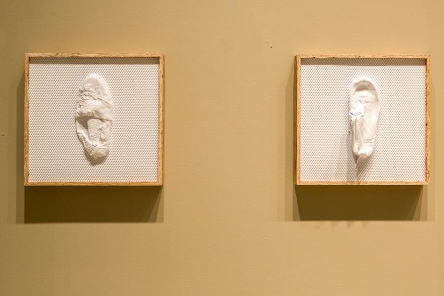 A pair of framed relief sculptures depicting abstracted white forms on a textured background, mounted on a beige wall.