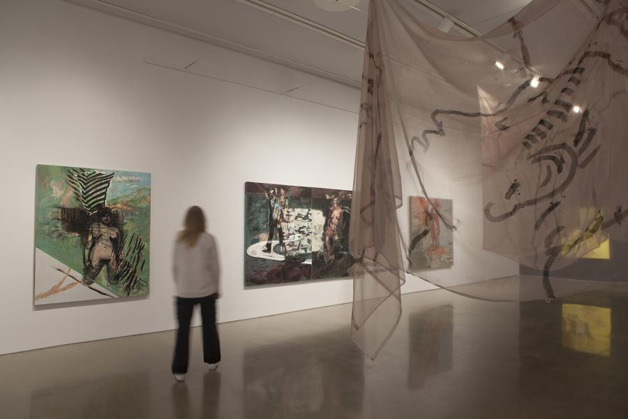 A visitor engaging with Sheila Butler’s layered paintings and ethereal hanging fabric installation, highlighting the interplay of space and materiality.