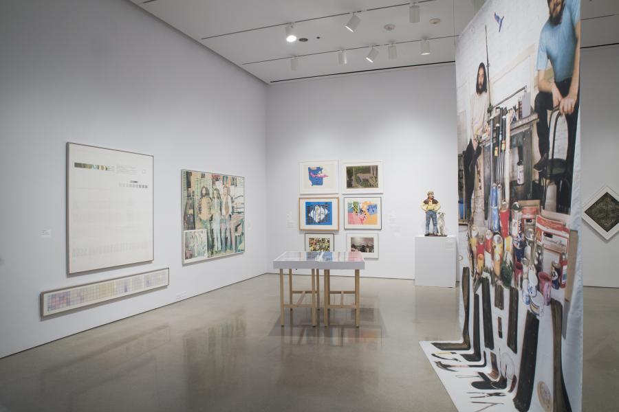 A gallery space with a mix of framed prints, colorful banners, sculptures, and display tables showcasing diverse artworks.