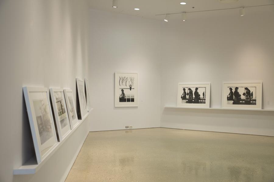 White-walled gallery with framed prints on a ledge and a larger artwork hung at the back.