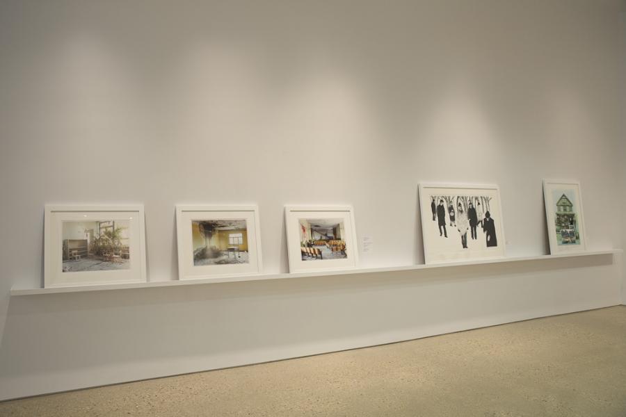 Framed artworks on a gallery ledge, featuring color photos and monochromatic graphics.