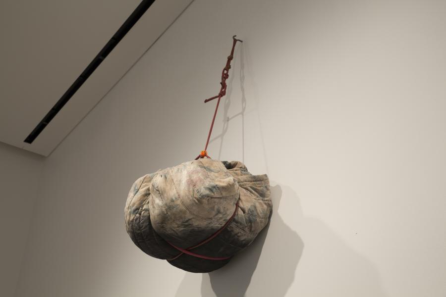A suspended fabric bundle, tightly wrapped and tied with red rope, hanging from a wall hook.