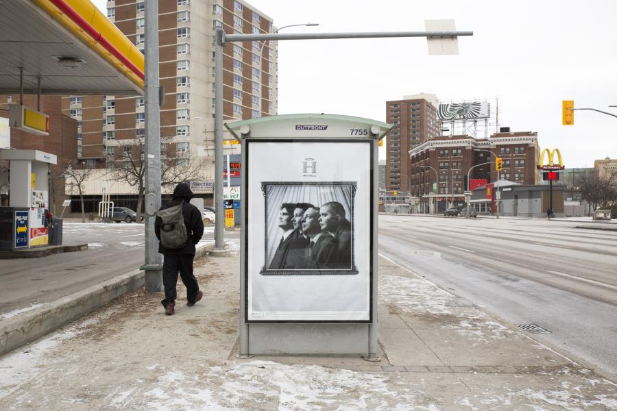 A city street bus shelter with a black-and-white portrait of three formally dressed individuals, framed in a vintage style. A pedestrian walks by with a backpack.