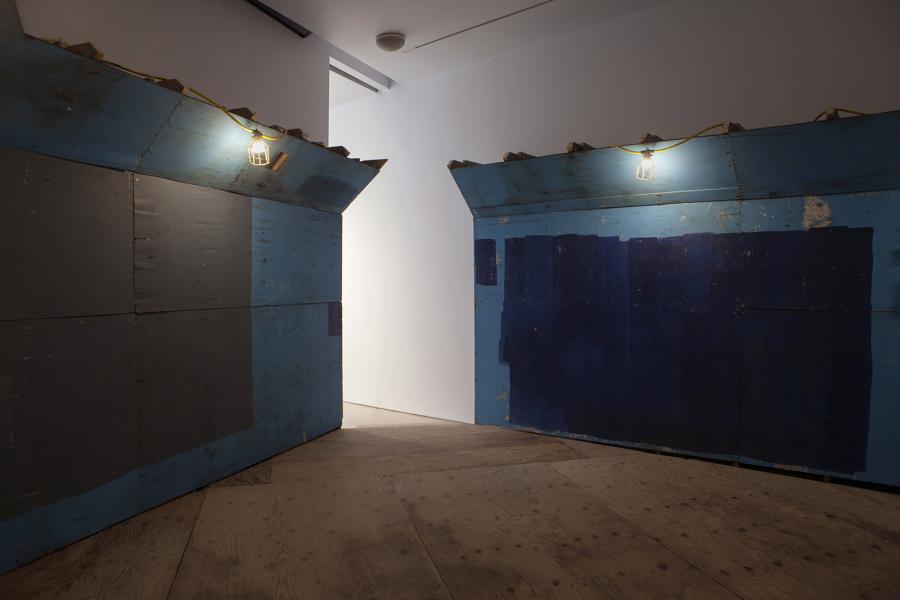A blue wooden structure with dim lighting and industrial-style lamps, resembling a passageway.