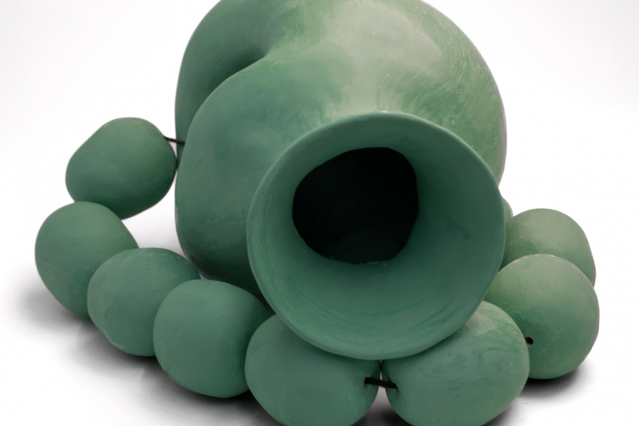A sculptural ceramic work resembling a green vessel surrounded by rounded organic forms.