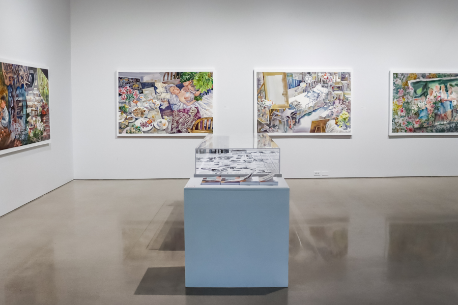 Gallery installation view of Xianghui Guan's MFA thesis exhibition "The Protagonist," featuring a series of large, colorful figurative paintings hung on white walls, with a central display case and artist books.