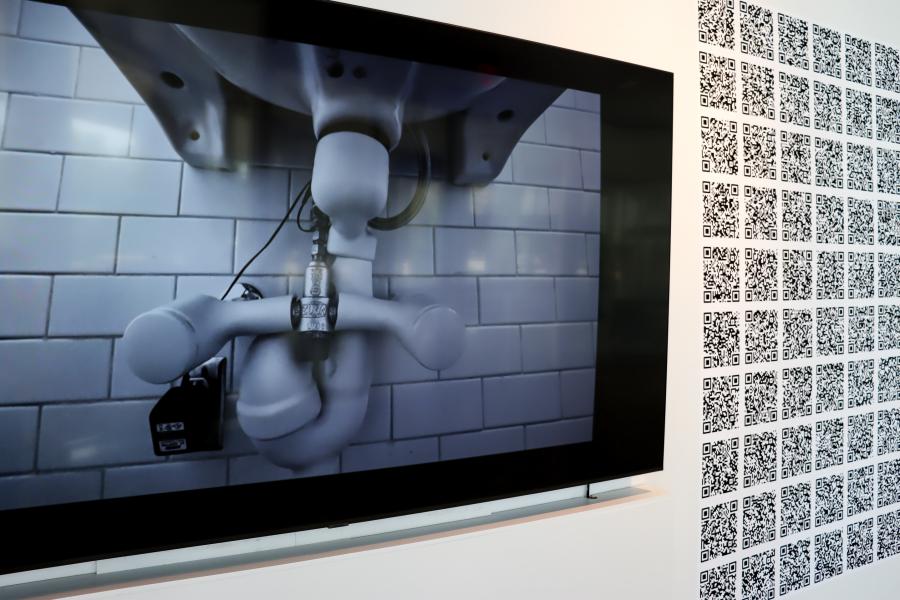 Video still showing complex plumbing and machinery in grayscale on a screen beside the QR code installation.