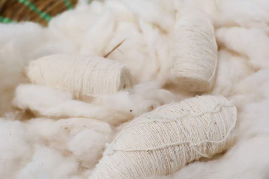 Close-up of raw cotton and handspun white yarn bundles placed in a green woven basket, highlighting natural fibre use and manual labor traditions in textile production.
