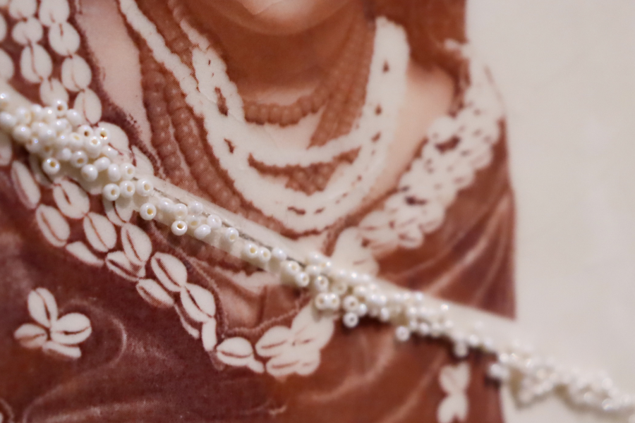 Detail of beadwork stitched across a ceramic photograph transfer, emphasizing the texture and intricacy of layered necklaces in the original image.