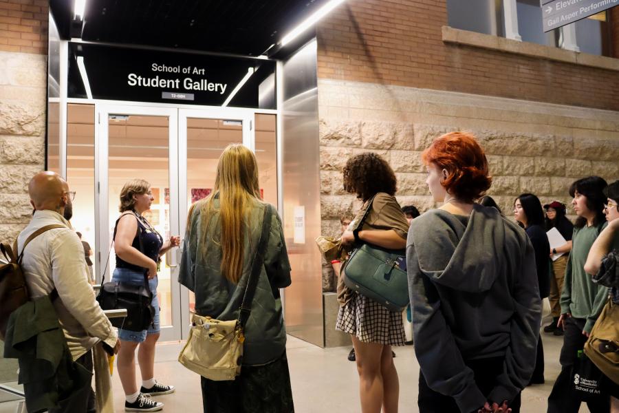 A group of students gathers outside the School of Art Student Gallery at the University of Manitoba during a guided tour.
