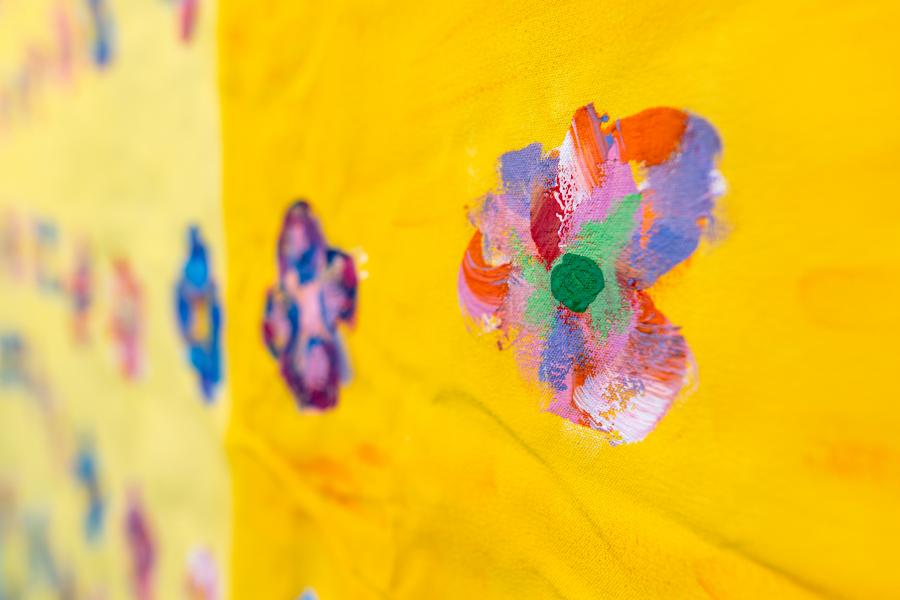 Detail of painted fabric with multicoloured flower-like marks on bright yellow.