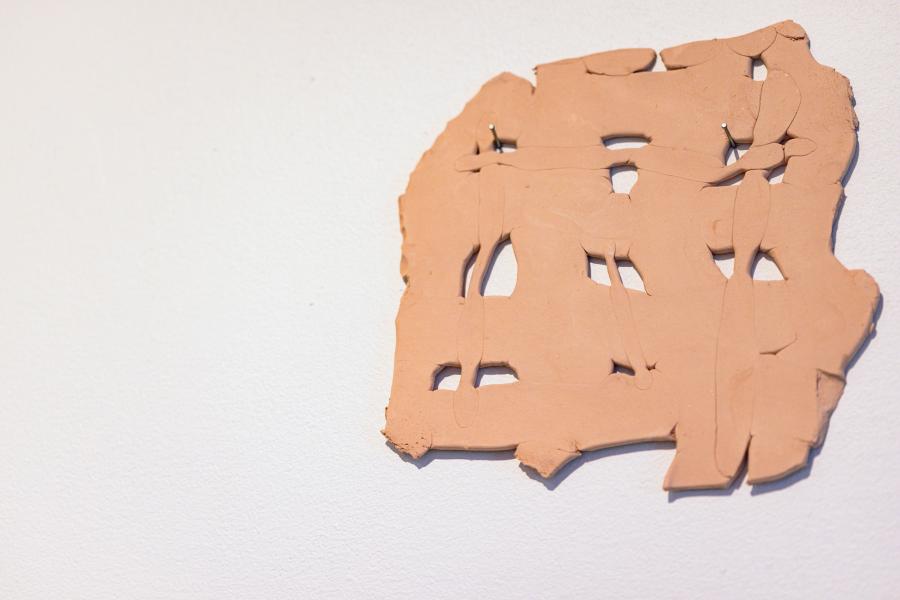 Textured terracotta clay form with cut-out shapes mounted on a wall.