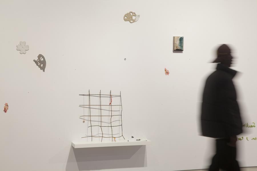 Blurred figure walking past wall-mounted ceramic and mixed-media works.