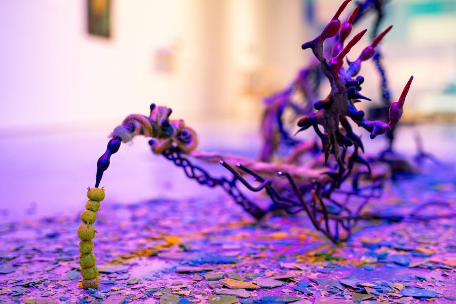 Twisted sculptural form with yellow beads and wool on a confetti-covered floor.