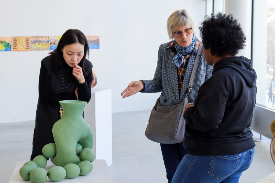 Faculty members and student engaged in a discussion around a green ceramic sculpture in a brightly lit gallery space.