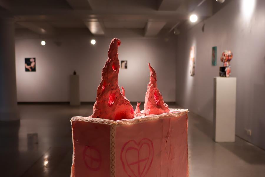 Pink sculptural forms rise from a box-like pedestal in the center of a gallery.