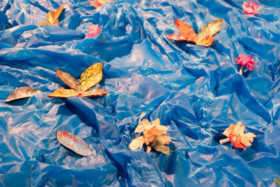 Small handmade flower forms scattered across crinkled blue plastic sheeting.
