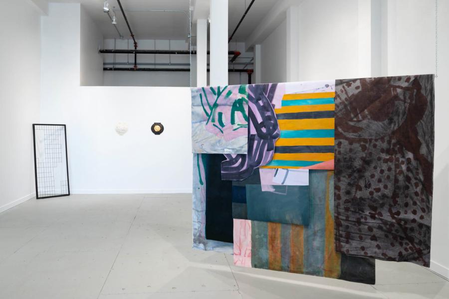 Large, suspended textile composition made of layered, painted fabric panels in varied colours and patterns, shown mid-installation.