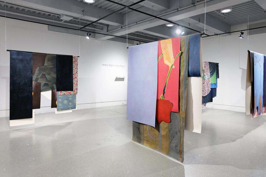 Gallery installation featuring large, hanging painted textiles arranged in rows, creating a rhythmic, immersive environment.