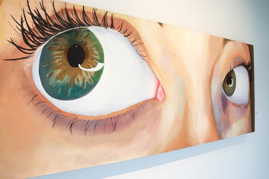 Large painting of a close-up face with wide green eyes, emphasizing eyelashes, skin tones, and an intense, direct gaze.