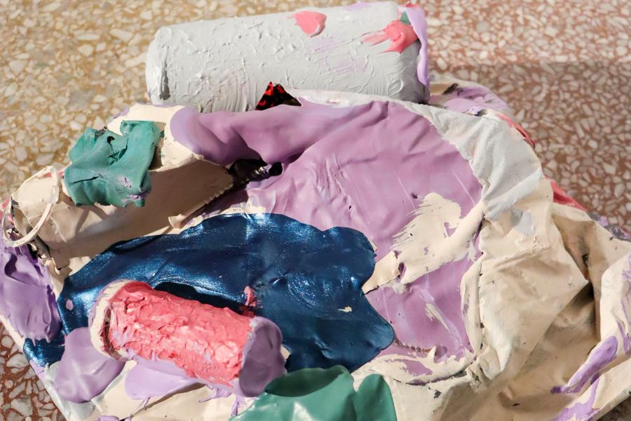 Abstract sculptural form covered in thick layers of pastel-colored paint on a speckled floor.