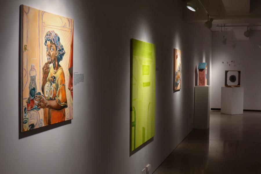 Gallery hallway with paintings hung along a wall and sculptural works displayed on pedestals in the distance.