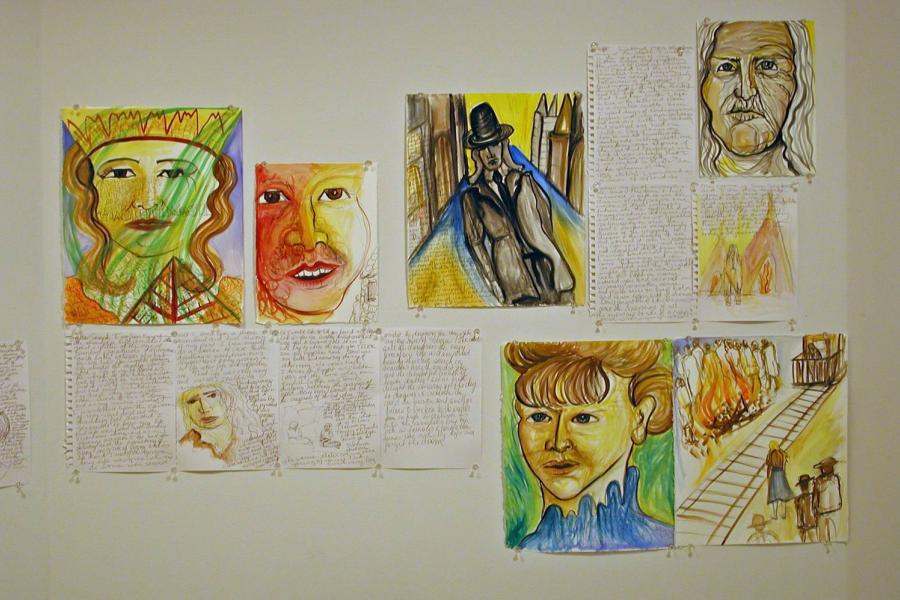 Thirteen notebook pages of handwriting and vibrant illustrations pinned on the gallery wall. Four fully illustrated pages depict faces, another depicts a suited figure walking alone in the street, and another depicts a large fire and crowd beside a railroad. One partially illustrated page depicts a face, another depicts a figure in front of two tipis, and another depicts two seated figures in blackline.