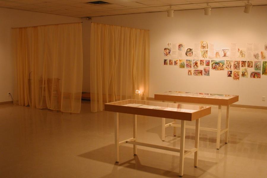 The gallery. The corner is sectioned off by translucent yellow curtains, with furniture visible behind them. To the right, many notebook pages of writing and vibrant illustrations are pinned on the wall. Most are illustrations of faces. Two display cases sit in front of the wall, with reflected light obscuring their contents.