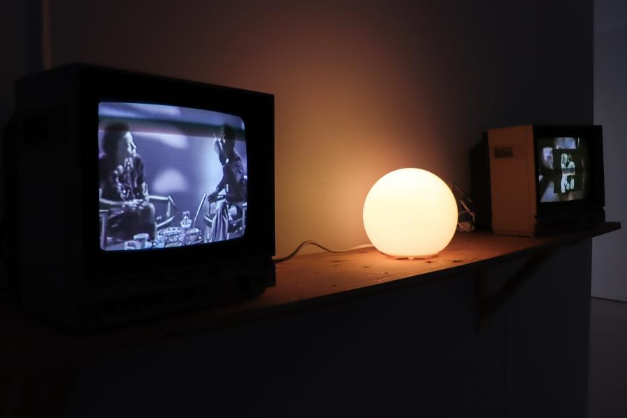 Vintage CRT televisions playing archival video beside a glowing lamp.